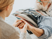 Junge Frau hält einem älteren Patienten die Hand