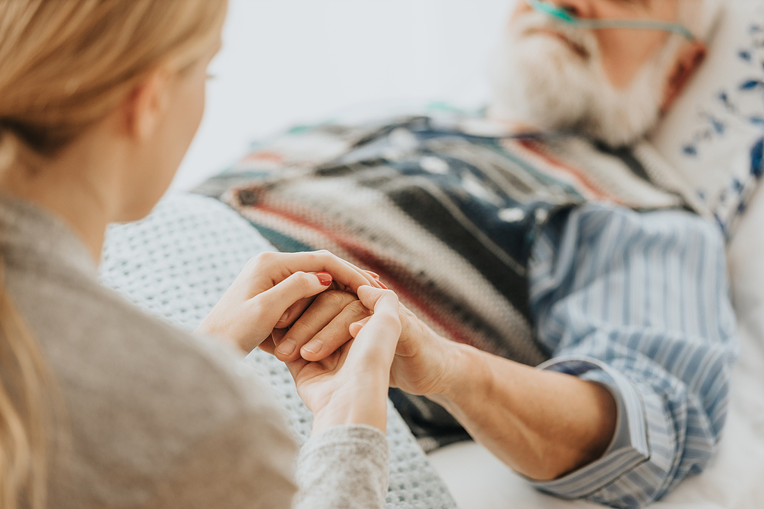 Junge Frau hält einem älteren Patienten die Hand